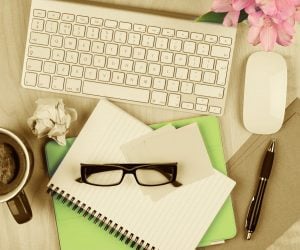 Messy office table with notepad, computer, reading glasses and coffee cup. View from above with copy space